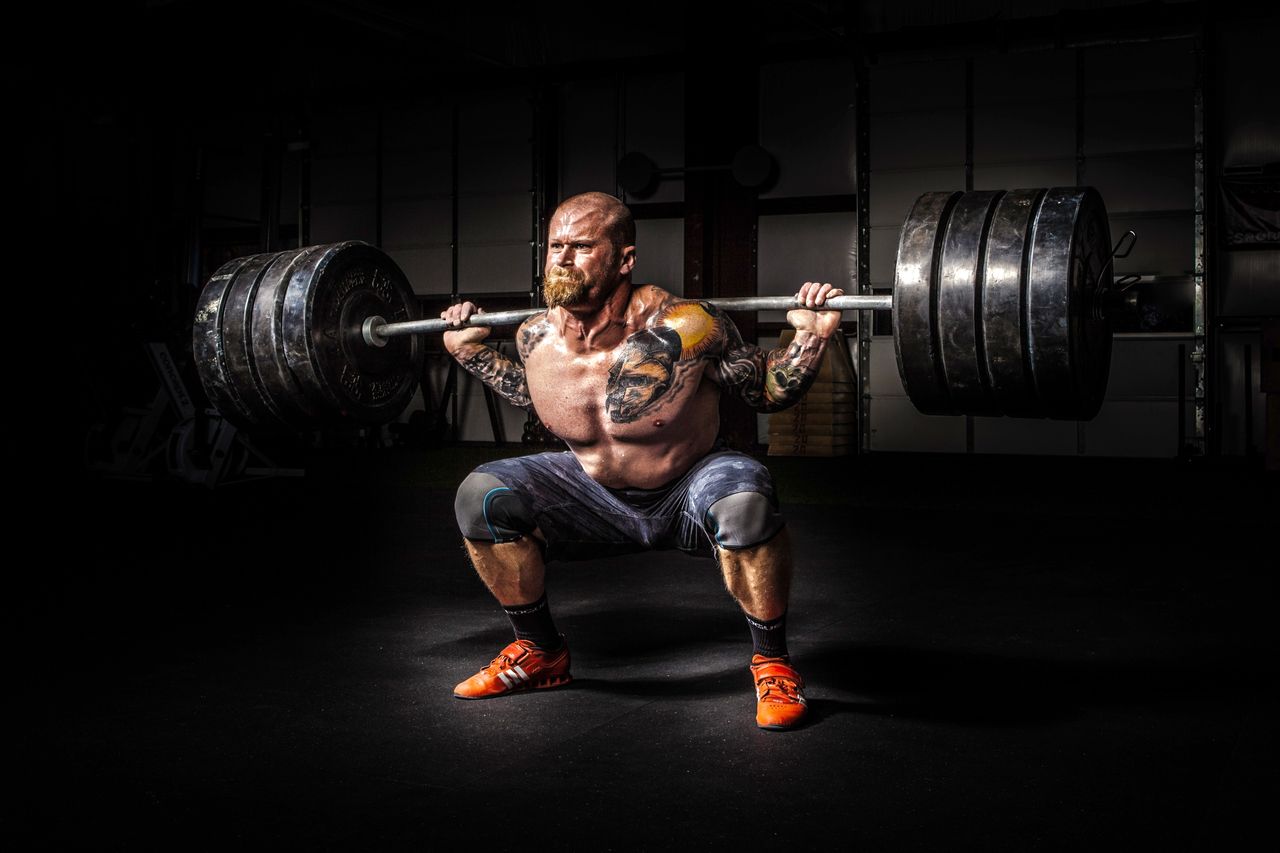 Muscular man lifting heavy weights during an intense squat session inside a gym.